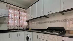 Une cuisine de taille réduite équipée d’un lave-linge, d’une cuisinière et de placards.