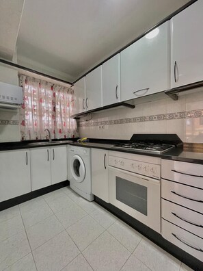 A compact kitchen with a washing machine, a stove, and cabinets.