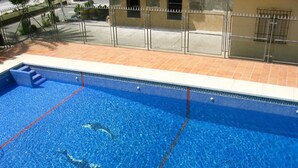 Une piscine à l’eau d’un bleu limpide, une terrasse carrelée et une clôture en métal.