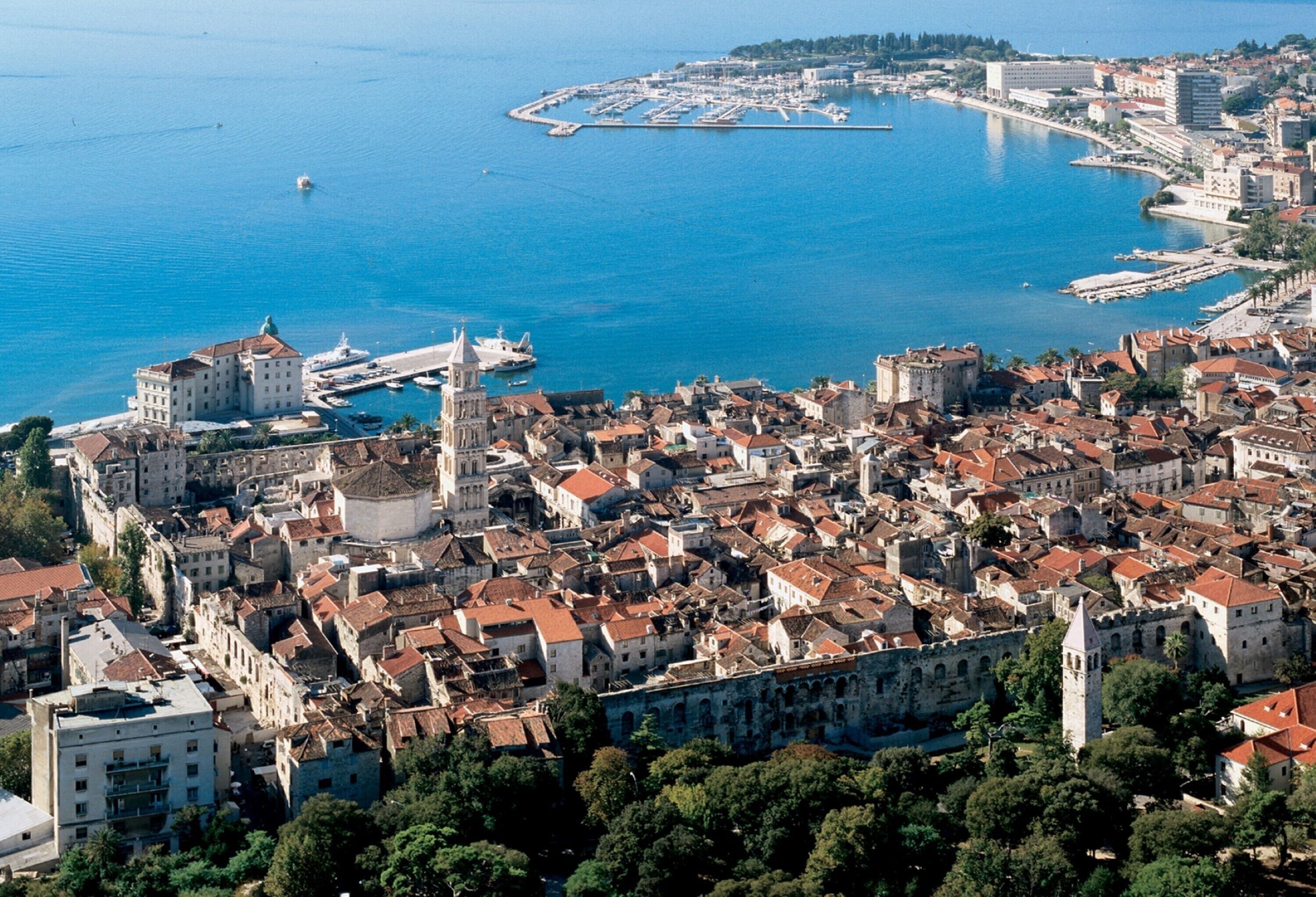 An aerial view of a coastal city with historic buildings, a marina, and a prominent church.