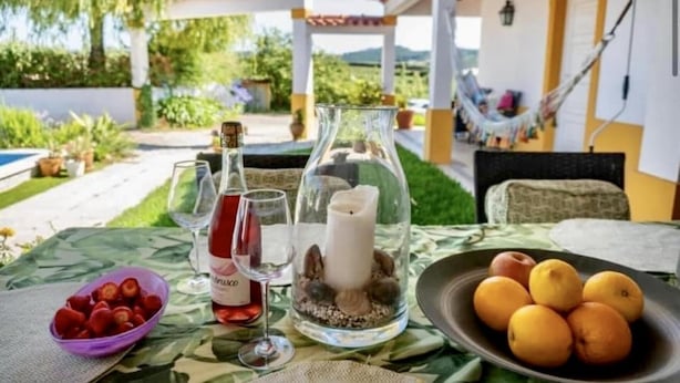 A table set with a bottle of wine, glasses, a candle, and a bowl of fruit. - Farmhouse Sleeps 8 With Pool & Horses (Alcobaça)