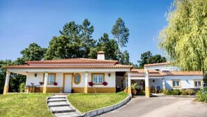 A two-story house with a tiled roof, a front porch, and a driveway leading to the entrance. - Farmhouse Sleeps 8 With Pool & Horses (Alcobaça)