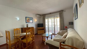 Un saló amb un sofà, cadires de fusta, una taula de dinar, un televisor i una finestra amb cortines.