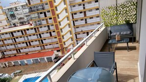 A balcony with a glass table and chairs, a small pool, and a view of a multi-story building. - TERRASOL ESTRELLA 6 (Torre del Mar)