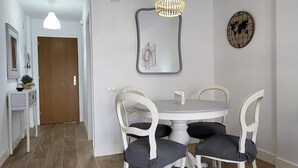 A dining area with a round table and four chairs, a hanging light fixture, a wall clock, and a door in the background. - TERRASOL ESTRELLA 6 (Torre del Mar)
