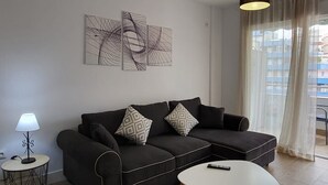 A modern living room with a dark sofa, two patterned throw pillows, a white coffee table, and abstract wall art. - TERRASOL ESTRELLA 6 (Torre del Mar)