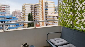 A balcony with a view of city buildings, a small table with a box, and a cushioned bench. - TERRASOL ESTRELLA 6 (Torre del Mar)