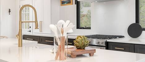 A modern kitchen with a white countertop, a gas stove, a wooden cutting board, and an artichoke centerpiece.