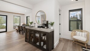 A modern kitchen with a central island, large windows, and a dining area with chairs. - Stunning Lake Views near RMNP with Hot Tub (Grand Lake)