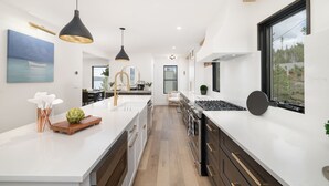 A modern kitchen with white countertops, dark cabinetry, and pendant lighting. - Stunning Lake Views near RMNP with Hot Tub (Grand Lake)