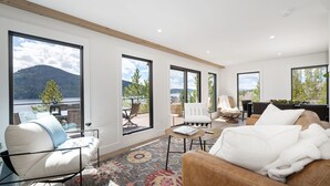 A modern living room with large windows, a sofa, a chair, and a coffee table. - Stunning Lake Views near RMNP with Hot Tub (Grand Lake)