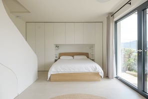Un dormitorio moderno con una cama grande, almacenamiento integrado y una puerta corrediza de vidrio a un balcón.