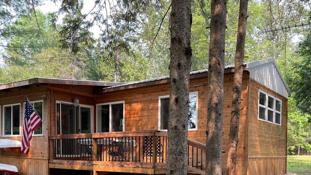 A wooden cabin with a deck, surrounded by trees.