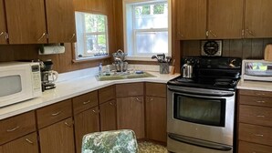 A compact kitchen with wooden cabinets, a microwave, a stove, and a sink.