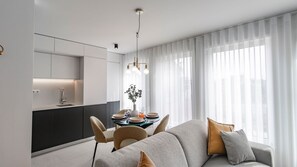 A modern living room with a sofa and chairs, a dining table with plates and glasses, and a kitchen area with cabinets and a sink. - Downtown Bliss w/ AC by LovelyStay (Porto)