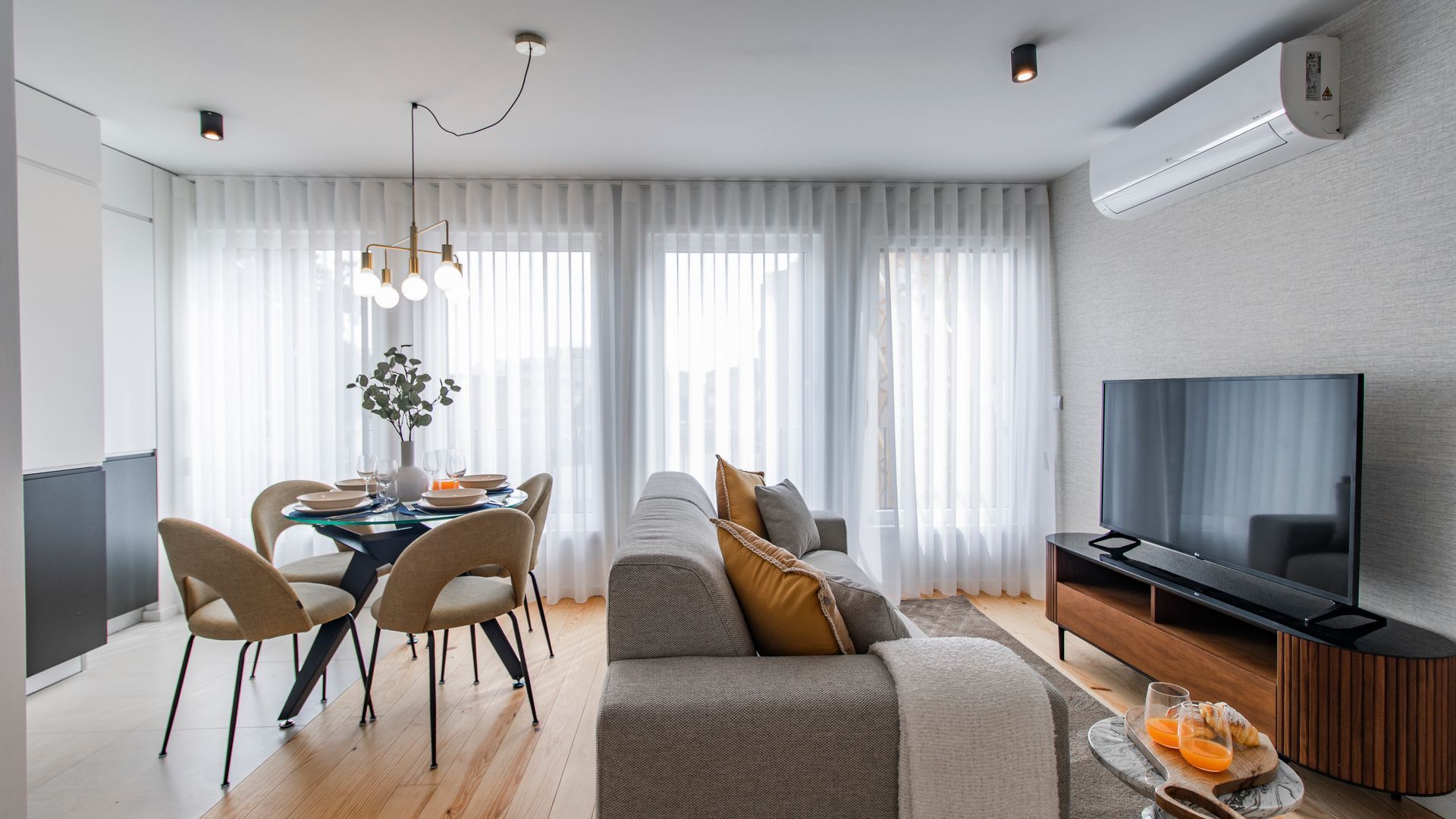 A modern living room with a dining area, a sofa, a TV, and a dining table with chairs.
