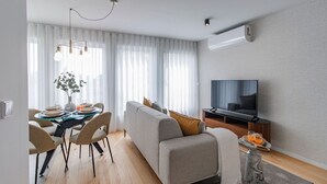 A modern living room with a sofa, TV, dining table, and a plant. - Downtown Bliss w/ AC by LovelyStay (Porto)