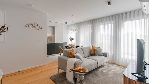 A modern living room with a grey sofa, wooden flooring, and a flat-screen TV. - Downtown Bliss w/ AC by LovelyStay (Porto)