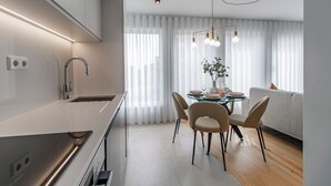 A modern kitchen with a built-in oven, a stainless steel sink, and a dining area with a glass table and four chairs. - Downtown Bliss w/ AC by LovelyStay (Porto)