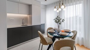 A modern kitchen with a built-in oven, a dining area with a glass table, and a large window with sheer curtains. - Downtown Bliss w/ AC by LovelyStay (Porto)