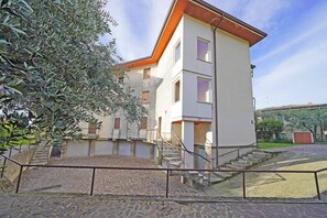 A multi-story building with a stone-paved courtyard, a staircase, and a metal railing. - Casa Peler - Gardagate (Toscolano-Maderno)