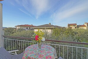 A balcony with a table, a railing, and a view of houses and greenery. - Casa Peler - Gardagate (Toscolano-Maderno)