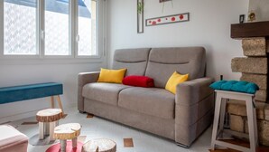 Una sala de estar con un sofá gris, cojines coloridos, un banco azul y un taburete de madera.