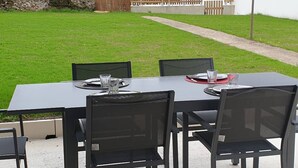 Un espacio al aire libre con zona de comedor, una mesa, sillas, un muro de piedra y una valla de madera al fondo.