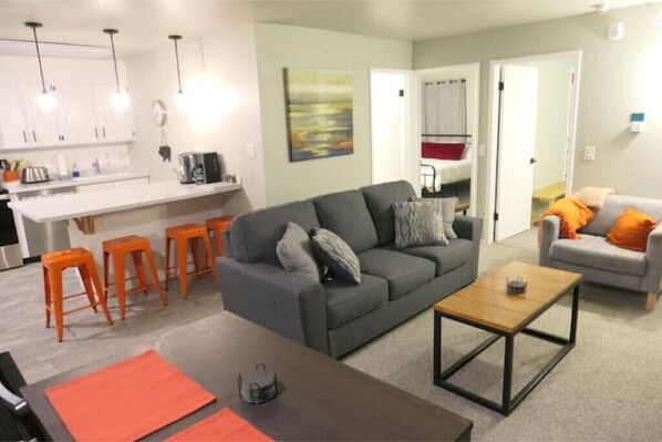 A modern living room with a grey sofa, orange stools, and a coffee table.