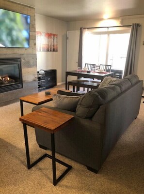 A living room with a gray sofa, a wooden coffee table, a fireplace, and a dining area with a table and chairs.
