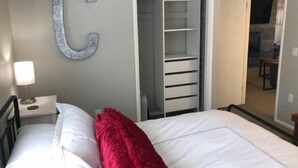 A bedroom with a bed, a nightstand, a lamp, a closet, and a large C-shaped wall decoration. - Summer at Resort - Pool, Hot Tub, Sauna, AC & Gym (Park City)