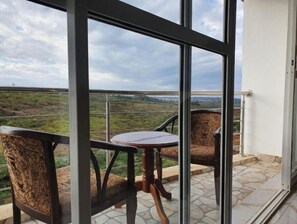 A balcony with a table and two chairs, overlooking a landscape with greenery and distant hills. - Greenzone BnB (Kiambu County)