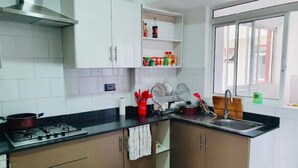 A kitchen with a gas stove, cabinets, a window, and a shelf with condiments. - Greenzone BnB (Kiambu County)
