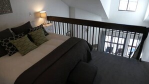 Ein Schlafzimmer mit Bett, Nachttisch, Lampe und Blick ins Freie durch ein Fenster.