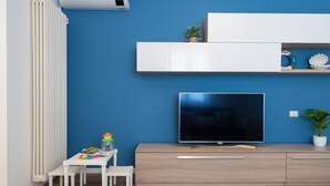 A modern living room with a blue wall, white furniture, a flat-screen TV, and a small table with toys. - Nida 18 - Two Bedroom Apartment, Sleeps 6 (Cattolica)