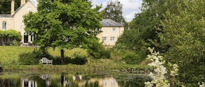 A house with a pond in front, surrounded by lush greenery and trees. - Colleton East Wing - Three Bedroom Villa, Sleeps 6 (Rackenford)