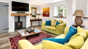 Ein Wohnzimmer mit gelbem Sofa, einem roten Teppich mit Muster, einem Holztisch und einem an der Wand befestigten Fernseher.