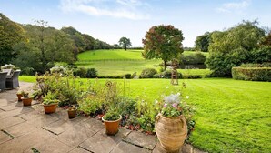 Ein gepflegter Garten mit Rasen, Blumentöpfen und einer Sitzgruppe mit Stühlen.