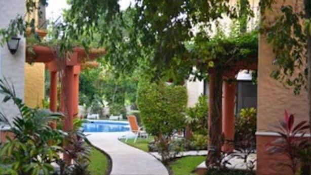 Un sendero conduce a una zona de piscina rodeada de follaje y columnas arquitectónicas.