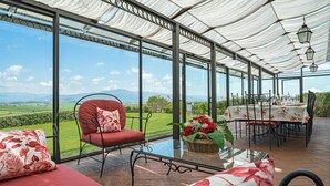 A conservatory with a glass table set for dining, a red cushioned chair, and a view of the countryside. - Villa Mimi - Nine Bedroom Villa, Sleeps 18 (Castroncello)
