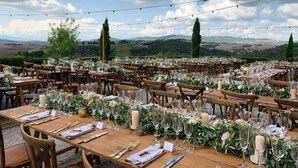 An outdoor dining area with tables set for a meal, surrounded by greenery and overlooking a scenic landscape.