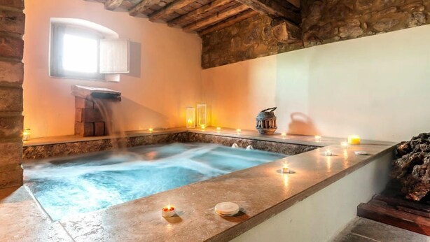 A spa area with a hot tub, candles, and a stone wall.