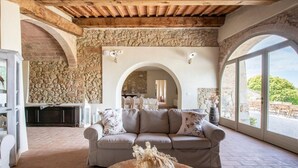 A cozy living room with a stone wall, a wooden ceiling, and a large window offering a view of the outdoors.