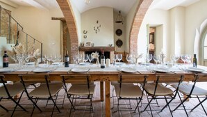 A long dining table set for a meal with chairs, a brick fireplace, and a stone wall in the background.