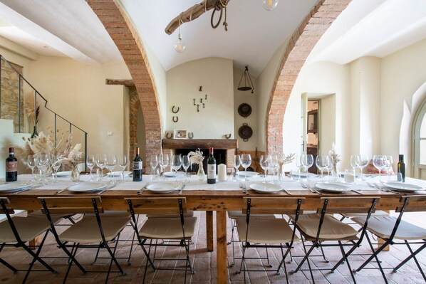 A long dining table set for a meal with chairs, a brick fireplace, and a stone wall in the background.