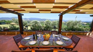 An outdoor dining area with a table set for six, surrounded by chairs, under a wooden pergola with a view of a rural landscape. - Villa Faruffini - Four Bedroom Villa, Sleeps 8 (Magliano Sabina)