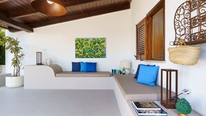 A modern living room with a curved sofa, a wall-mounted painting, a woven basket, and a small potted plant. - Camilla Canna - Three Bedroom Villa, Sleeps 6 (Cala Rossa)