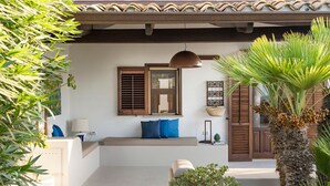 A modern outdoor seating area with a bench, a hanging pendant light, and potted plants. - Camilla Canna - Three Bedroom Villa, Sleeps 6 (Cala Rossa)