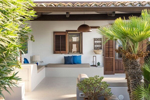 A modern outdoor seating area with a bench, a hanging pendant light, and potted plants.