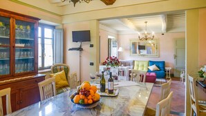 A dining area with a marble table, chairs, a fruit bowl, wine bottles, and a television. - Dimora Dayan - Nine Bedroom Villa, Sleeps 18 (Capannori)